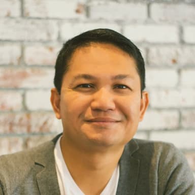 Southin Simphoukham, smiling, in a grey blazer against a white-painted brick wall